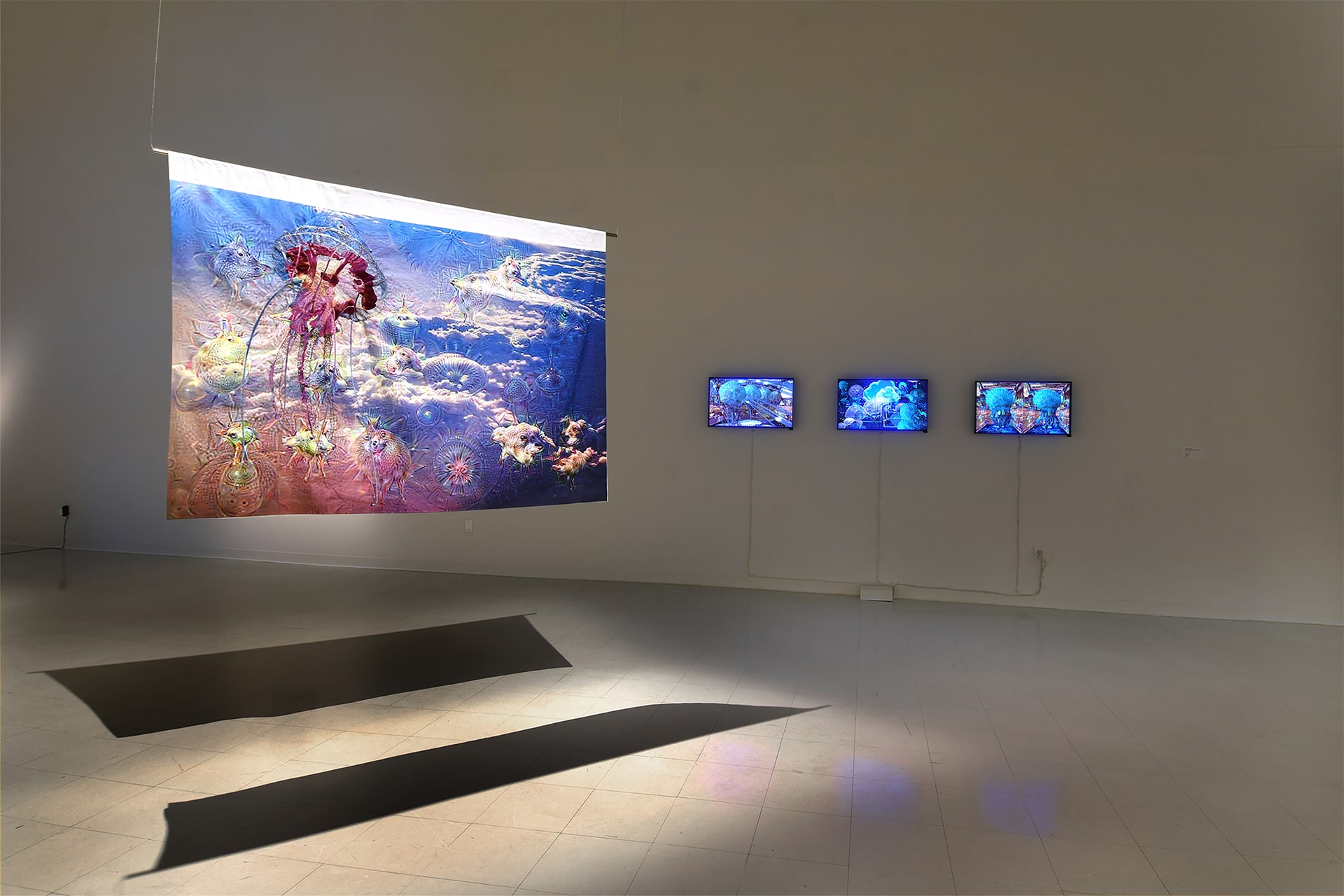 Untitled 1, large textile banner with hand embroidery of a jellyfish hanging from the ceiling next two three flatscreens on a wall